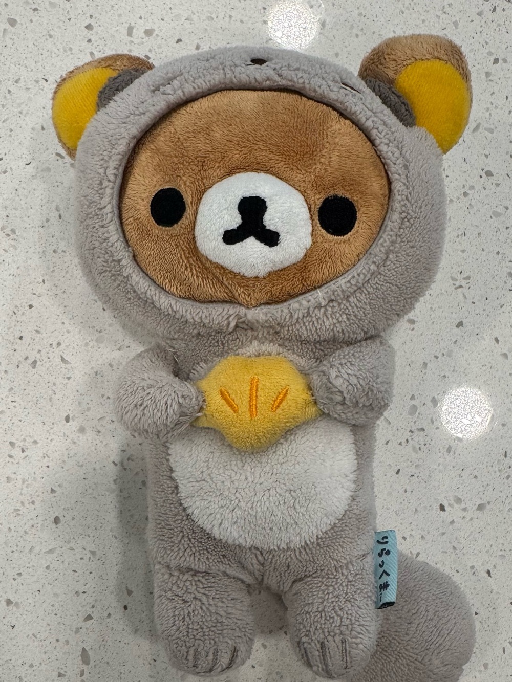 San-X Rilakkuma Style Plushy Wearing a Grey Sea Otter Costume With Yellow Shell